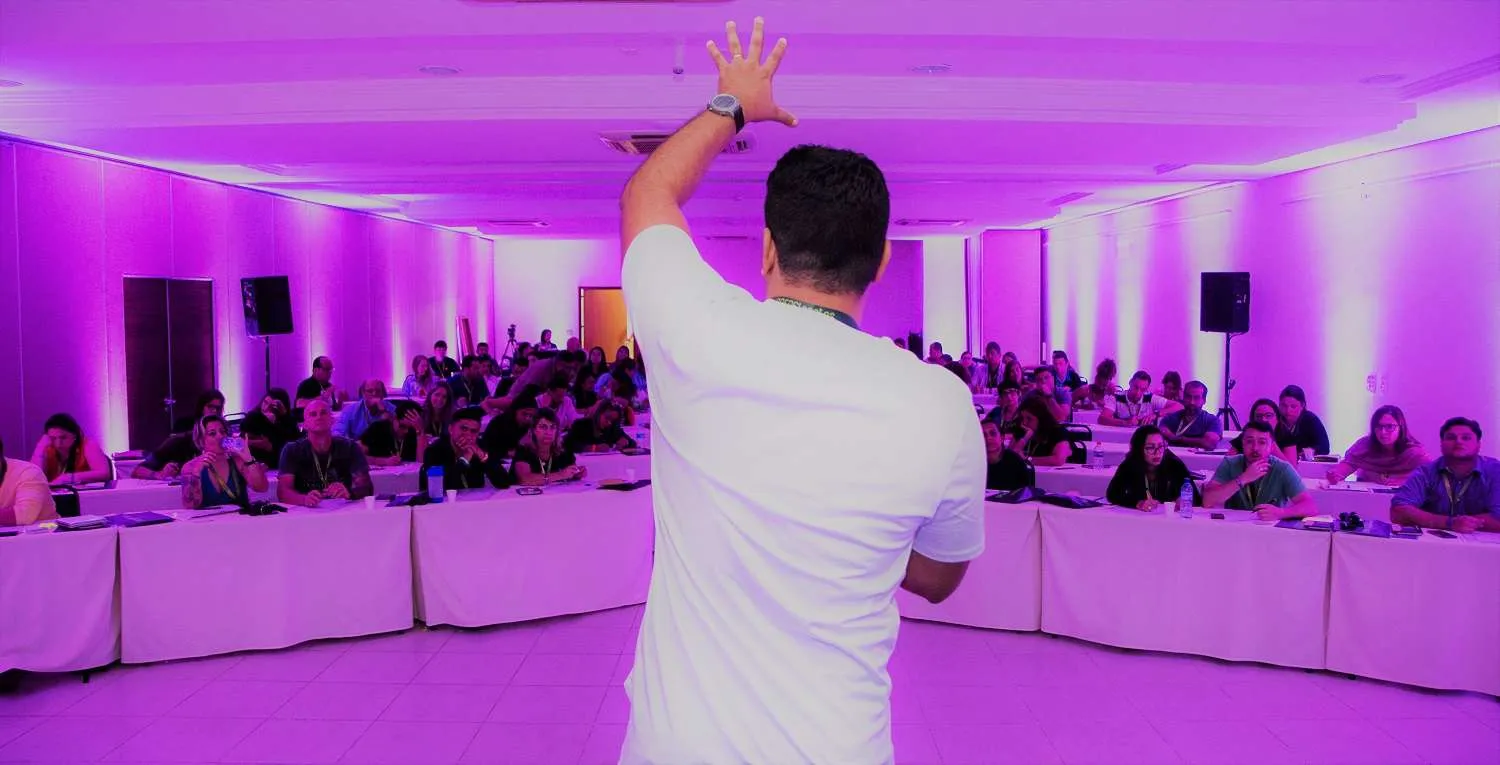 Rafael Santos palestrando em um evento com iluminação roxa para uma plateia atenta